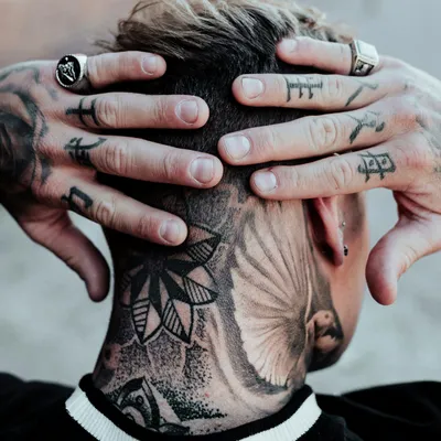 Mains tatouées posées sur une nuque tatouée d'un motif floral et d'une plume