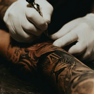Mains gantées tatouant un avant-bras déjà couvert d'un grand tatouage
